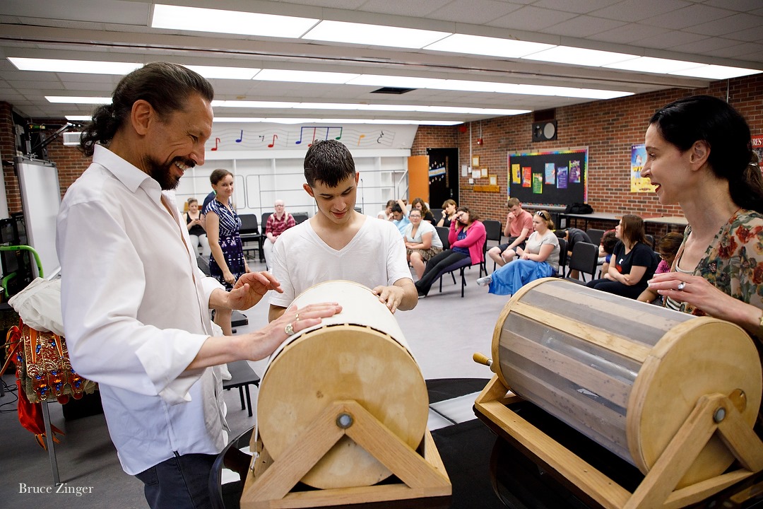 In a classroom, people gather around noise making cylinders on stands